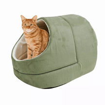 An orange tabby cat sitting inside a green Pets Paradise Elite Warming Burrow Suede Cat Cave Bed with a semi-enclosed design.